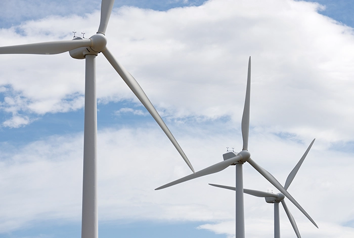 Three large wind turbines under a blue sky with white clouds, illustrating the article Indigenous Dialogue on Wind Energy: Insights from Brazil and Colombia.