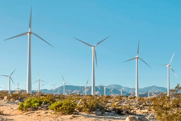 Multiple large white wind turbines in a rocky desert landscape under a blue sky, illustrating the research on how social resistance impacts the implementation of renewable energy in the Global South.